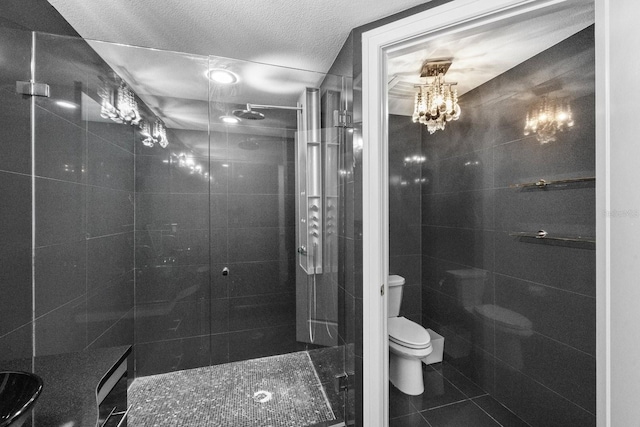 full bath with tile walls, toilet, a shower stall, a textured ceiling, and tile patterned flooring