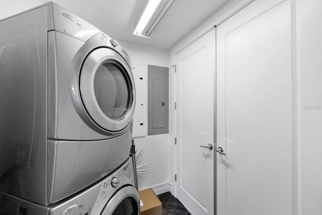 laundry room with laundry area, dark tile patterned flooring, stacked washer / dryer, and electric panel