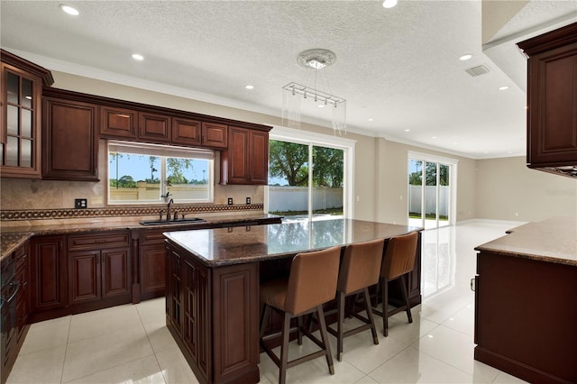 kitchen featuring sink, tasteful backsplash, a center island, light tile patterned floors, and ornamental molding