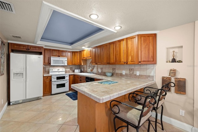 kitchen featuring light tile patterned flooring, sink, a raised ceiling, kitchen peninsula, and white appliances