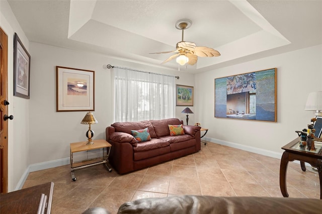 tiled living room with ceiling fan and a tray ceiling