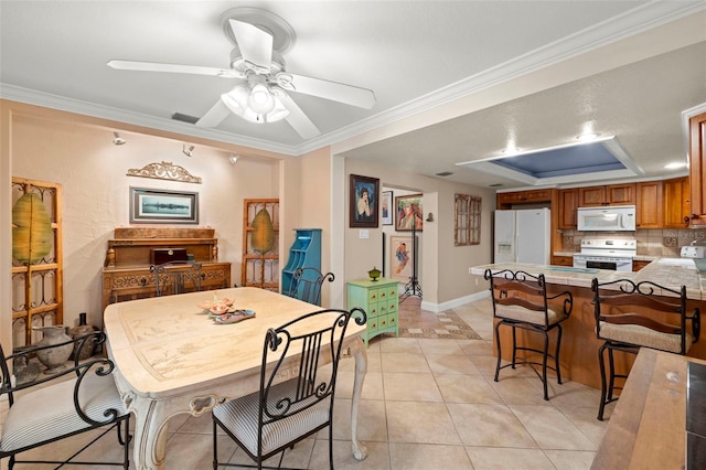 tiled dining space featuring a raised ceiling, crown molding, and ceiling fan