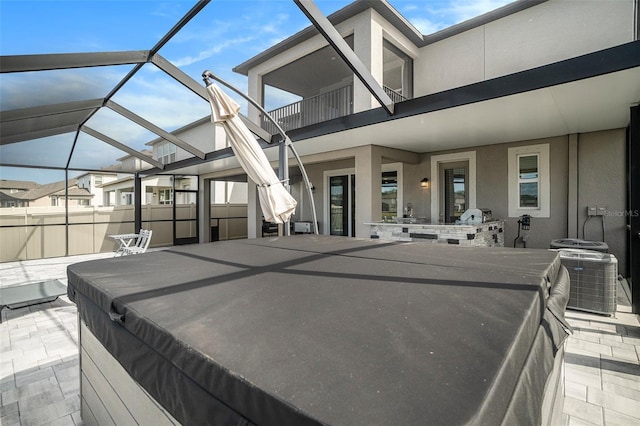 view of patio featuring a balcony, a hot tub, central AC unit, and a lanai