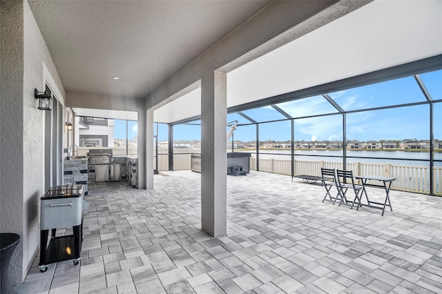 view of patio / terrace with a water view, area for grilling, a hot tub, a lanai, and exterior kitchen