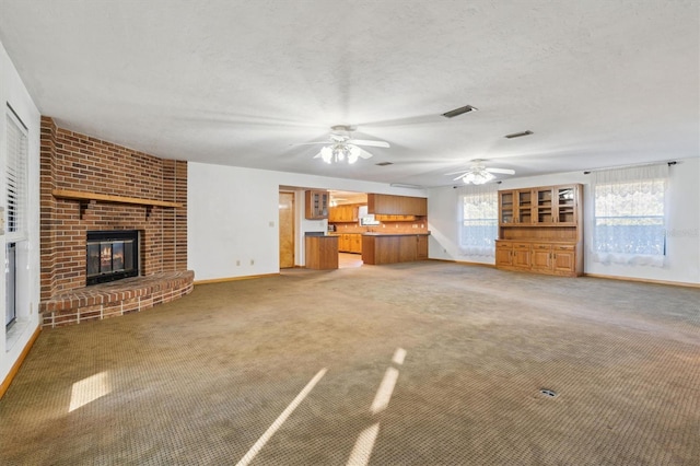 unfurnished living room featuring ceiling fan, carpet flooring, a brick fireplace, and a textured ceiling