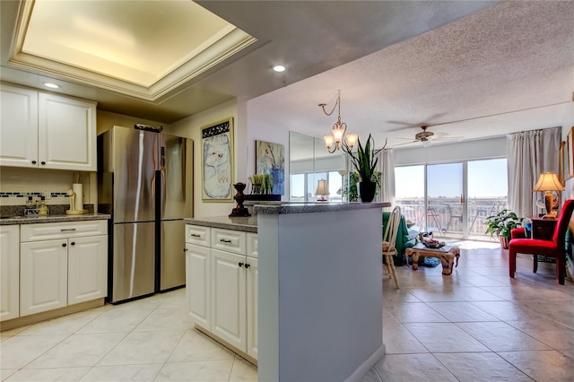 kitchen featuring a kitchen island, white cabinets, stainless steel fridge, a raised ceiling, and a textured ceiling