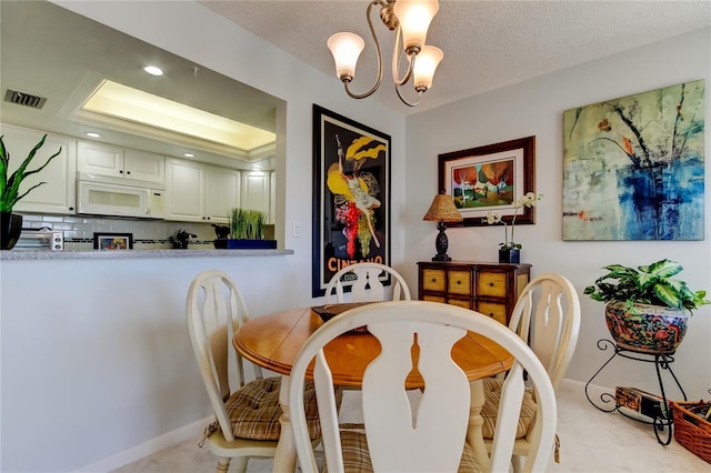 dining room featuring a chandelier, light colored carpet, a textured ceiling, and a tray ceiling