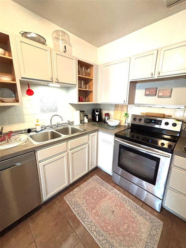 kitchen featuring appliances with stainless steel finishes, white cabinetry, sink, backsplash, and dark tile patterned floors