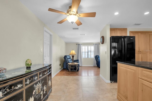 kitchen with light tile patterned floors, black refrigerator, light brown cabinets, ceiling fan, and dark stone counters