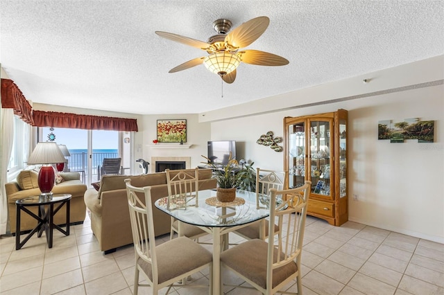 dining room with light tile patterned floors, a textured ceiling, a fireplace, and a ceiling fan