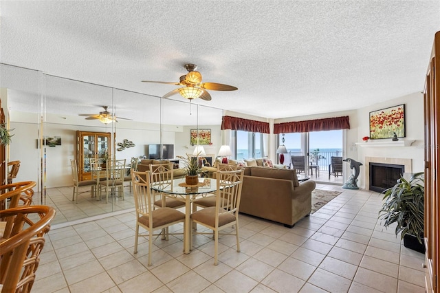 dining area featuring light tile patterned floors, ceiling fan, a fireplace, and a textured ceiling