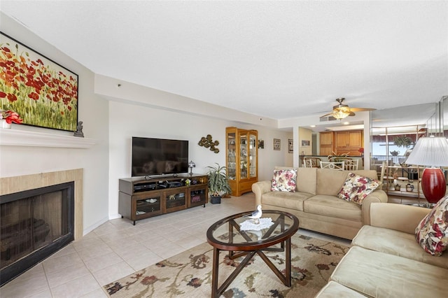 living room featuring ceiling fan, a textured ceiling, a tiled fireplace, and light tile patterned floors