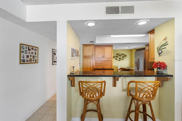 kitchen featuring a peninsula, a kitchen bar, visible vents, and stainless steel fridge with ice dispenser