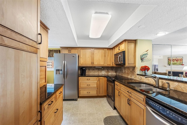 kitchen featuring a tray ceiling, stainless steel appliances, decorative backsplash, brown cabinetry, and a sink