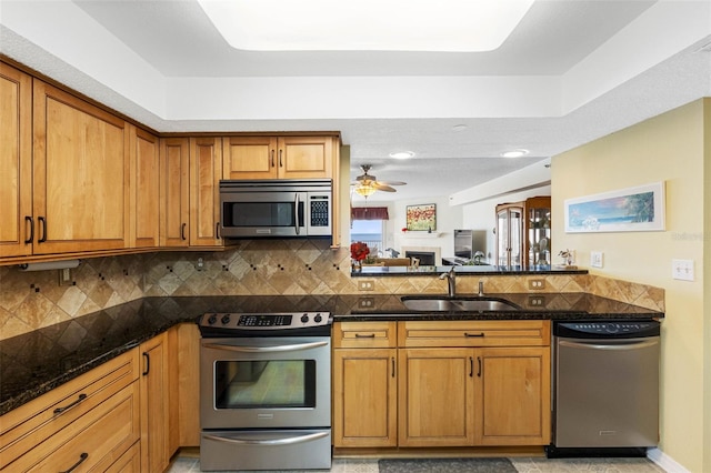 kitchen with decorative backsplash, appliances with stainless steel finishes, brown cabinets, dark stone countertops, and a sink