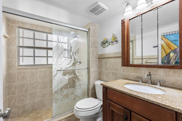 bathroom featuring tile walls, visible vents, toilet, a stall shower, and vanity