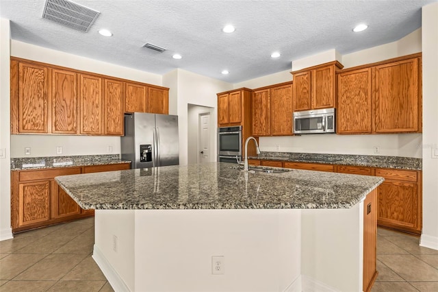 kitchen featuring stainless steel appliances, an island with sink, sink, and dark stone countertops