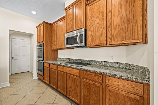 kitchen with stainless steel appliances, light tile patterned floors, a textured ceiling, and dark stone countertops