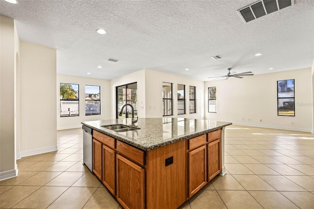 kitchen with stone countertops, sink, stainless steel dishwasher, light tile patterned floors, and a center island with sink