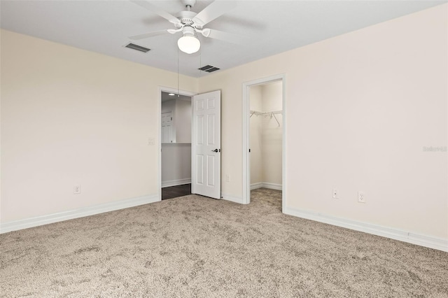 unfurnished bedroom with a walk in closet, a closet, ceiling fan, and carpet flooring