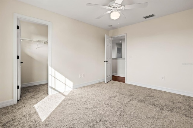 unfurnished bedroom featuring a walk in closet, a closet, ceiling fan, and carpet flooring