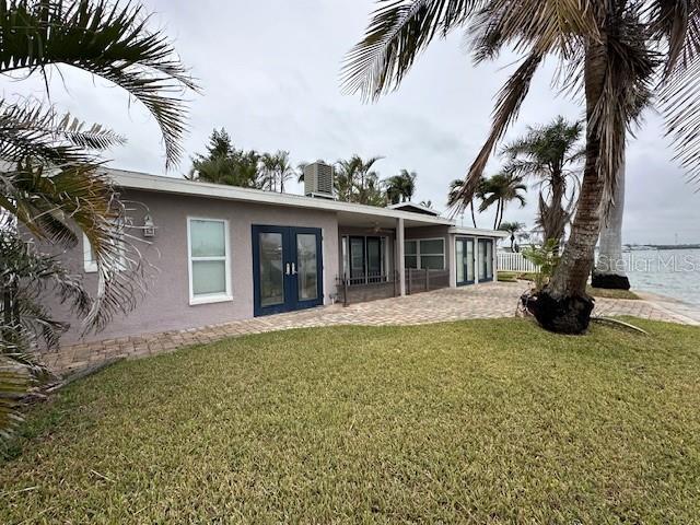 rear view of house featuring french doors, central AC, a patio area, a water view, and a lawn