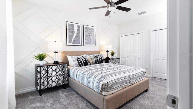 bedroom featuring dark carpet, ceiling fan, and two closets