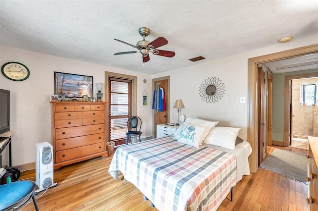 bedroom featuring a textured ceiling, a walk in closet, light hardwood / wood-style floors, and ceiling fan