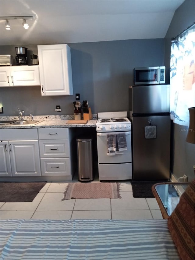 kitchen featuring sink, light tile patterned floors, appliances with stainless steel finishes, white cabinets, and vaulted ceiling