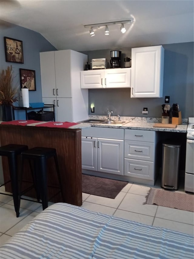 kitchen with light tile patterned floors, a kitchen breakfast bar, sink, and white cabinets