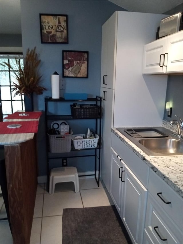 kitchen with sink, light tile patterned floors, white cabinets, and light stone counters