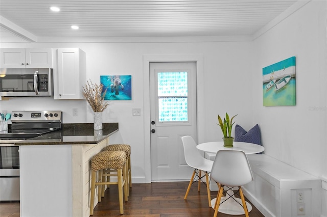 kitchen with appliances with stainless steel finishes, white cabinetry, dark stone counters, breakfast area, and dark wood-type flooring