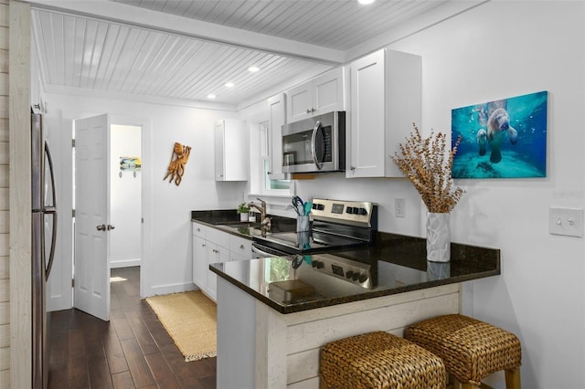 kitchen with appliances with stainless steel finishes, a breakfast bar area, white cabinets, kitchen peninsula, and beam ceiling