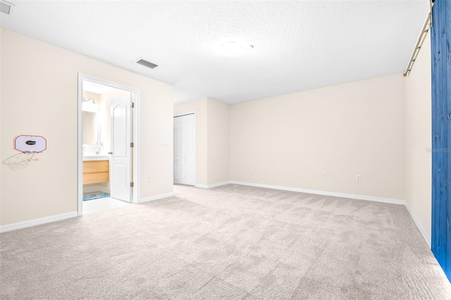 unfurnished bedroom featuring ensuite bathroom, light colored carpet, a textured ceiling, and a closet