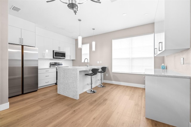 kitchen featuring a breakfast bar area, light hardwood / wood-style flooring, white cabinetry, stainless steel appliances, and decorative light fixtures