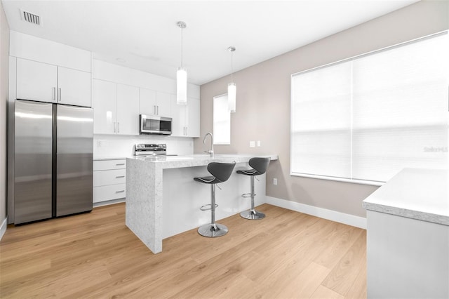 kitchen with pendant lighting, white cabinets, decorative backsplash, stainless steel appliances, and light wood-type flooring