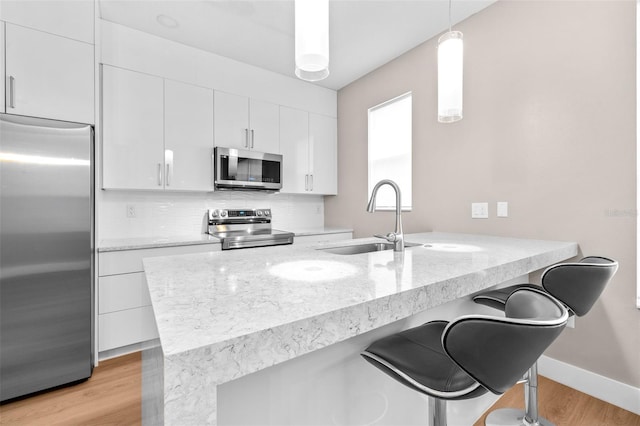 kitchen featuring decorative light fixtures, white cabinetry, sink, a breakfast bar area, and stainless steel appliances