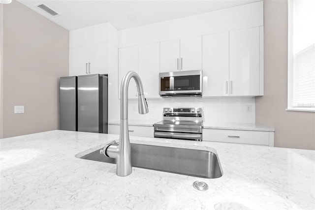 kitchen featuring sink, white cabinetry, backsplash, stainless steel appliances, and light stone counters