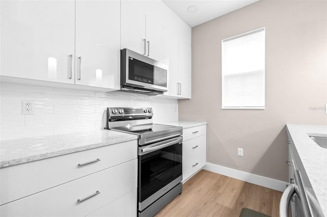 kitchen featuring light wood-type flooring, appliances with stainless steel finishes, a wealth of natural light, light stone countertops, and white cabinets