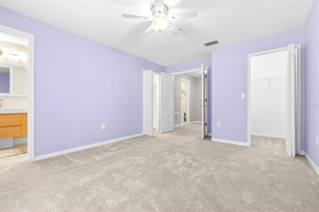 unfurnished bedroom with ceiling fan, connected bathroom, light carpet, a walk in closet, and a closet