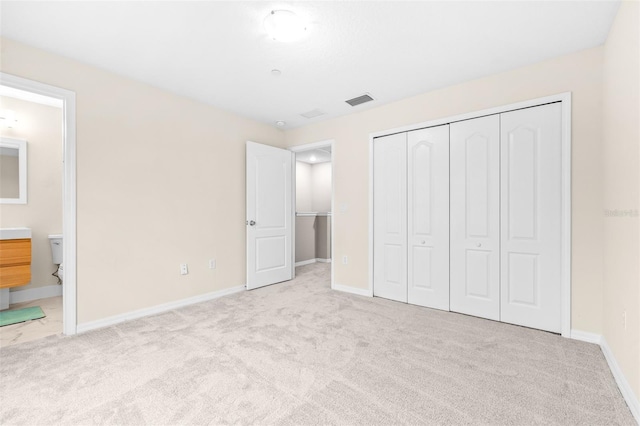 unfurnished bedroom featuring light colored carpet, a closet, and ensuite bathroom