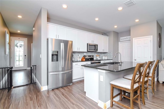 kitchen with stainless steel appliances, sink, white cabinets, and a kitchen island with sink