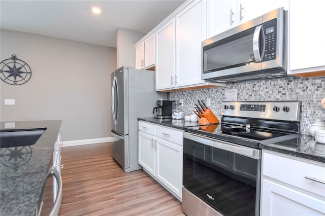 kitchen featuring light hardwood / wood-style flooring, stainless steel appliances, white cabinets, decorative backsplash, and dark stone counters