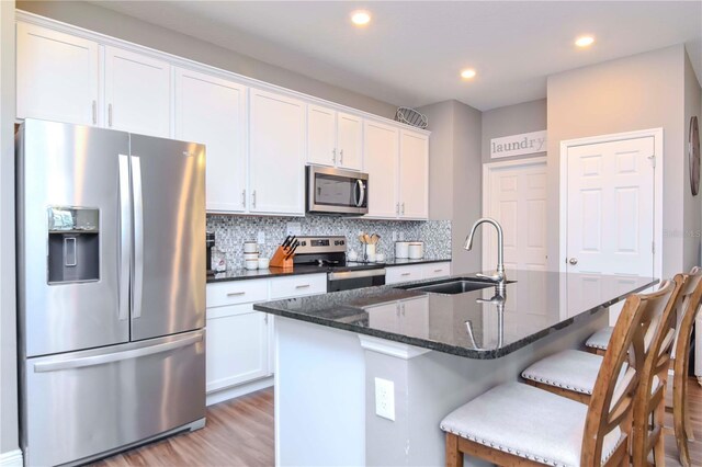 kitchen with sink, appliances with stainless steel finishes, tasteful backsplash, white cabinets, and a center island with sink