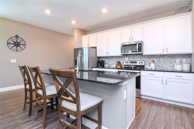 kitchen with white cabinetry, stainless steel appliances, dark wood-type flooring, and an island with sink