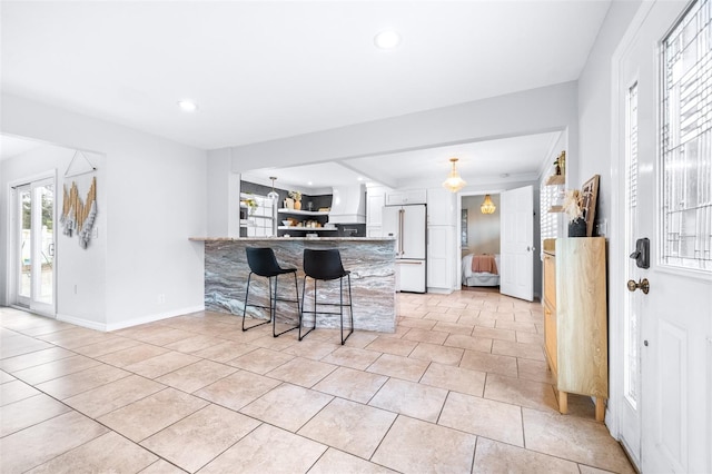 kitchen with light tile patterned floors, a kitchen breakfast bar, high end white refrigerator, white cabinets, and kitchen peninsula