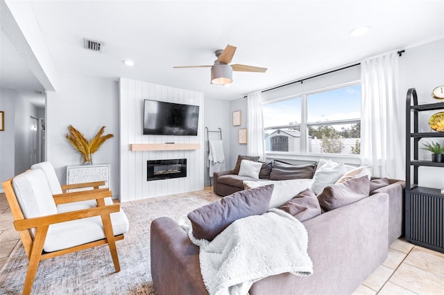 tiled living room with ceiling fan and a large fireplace