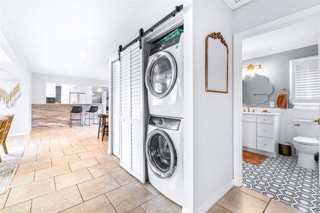 clothes washing area featuring sink, stacked washer and dryer, light tile patterned floors, and a barn door