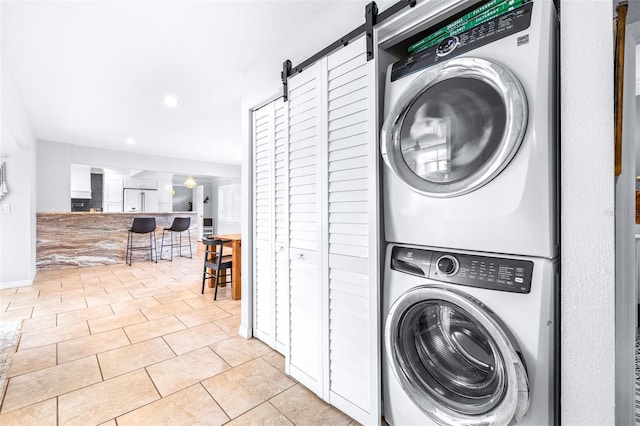 laundry area featuring stacked washer and dryer, a barn door, and light tile patterned floors