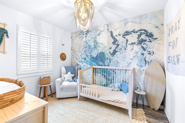 bedroom with a crib, wood-type flooring, and a chandelier